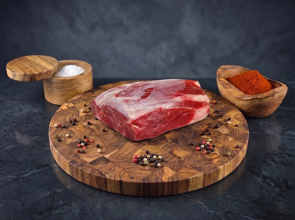 Raw steak on a wooden cutting board with salt, pepper, and spices on a dark background