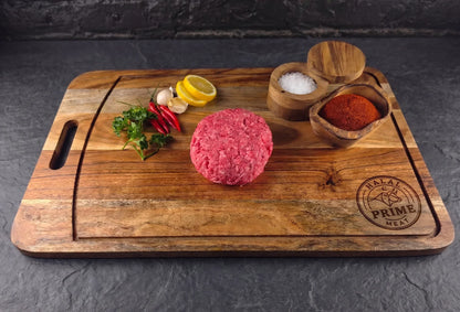 Raw hamburger patty on a wooden cutting board with spices and herbs.