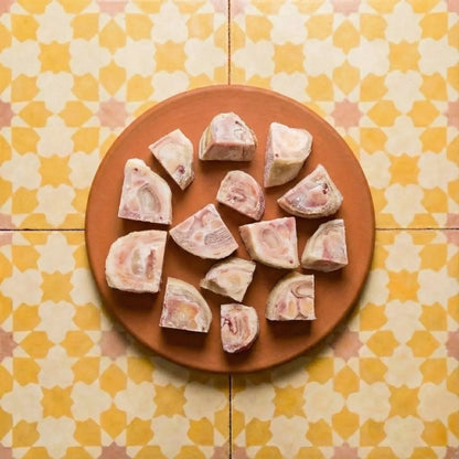 Raw Beef Cow Feet pieces with pink and white marbling on a terracotta plate atop yellow and cream quatrefoil patterned tiles