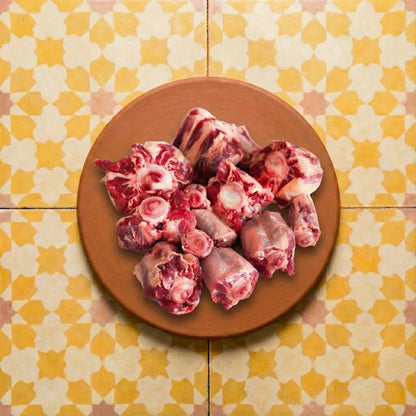 Terracotta platter holding raw oxtail cuts with deep red meat and white bone marrow, all resting on vibrant yellow and white star-patterned Moroccan Zellige tiles