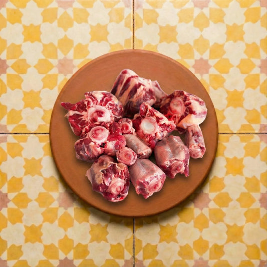 Terracotta platter holding raw oxtail cuts with deep red meat and white bone marrow, all resting on vibrant yellow and white star-patterned Moroccan Zellige tiles