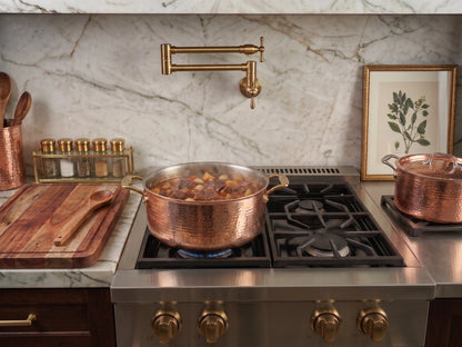 copper pot on a stove top with bone in goat stew