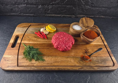 Wooden cutting board with raw extra lean ground beef, herbs, and spices on a dark surface.