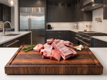 Raw lamb ribs arranged on a large wooden cutting board in a modern kitchen setting