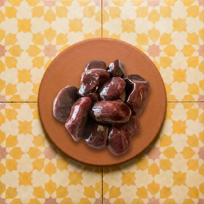Photograph of glistening dark red meat on a rustic terracotta plate set against a vibrant yellow and white geometric Moroccan zellige tile background