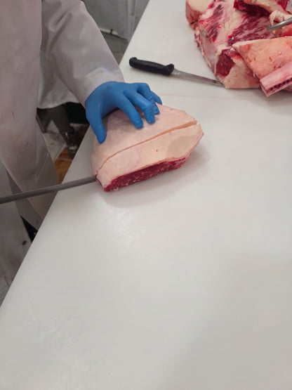 Photograph of a butcher slicing marbled beef on a white industrial cutting board in a professional kitchen featuring a bright blue nitrile glove and a long silver blade