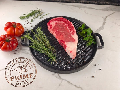 Ribeye steak on a grill pan with tomatoes and herbs.