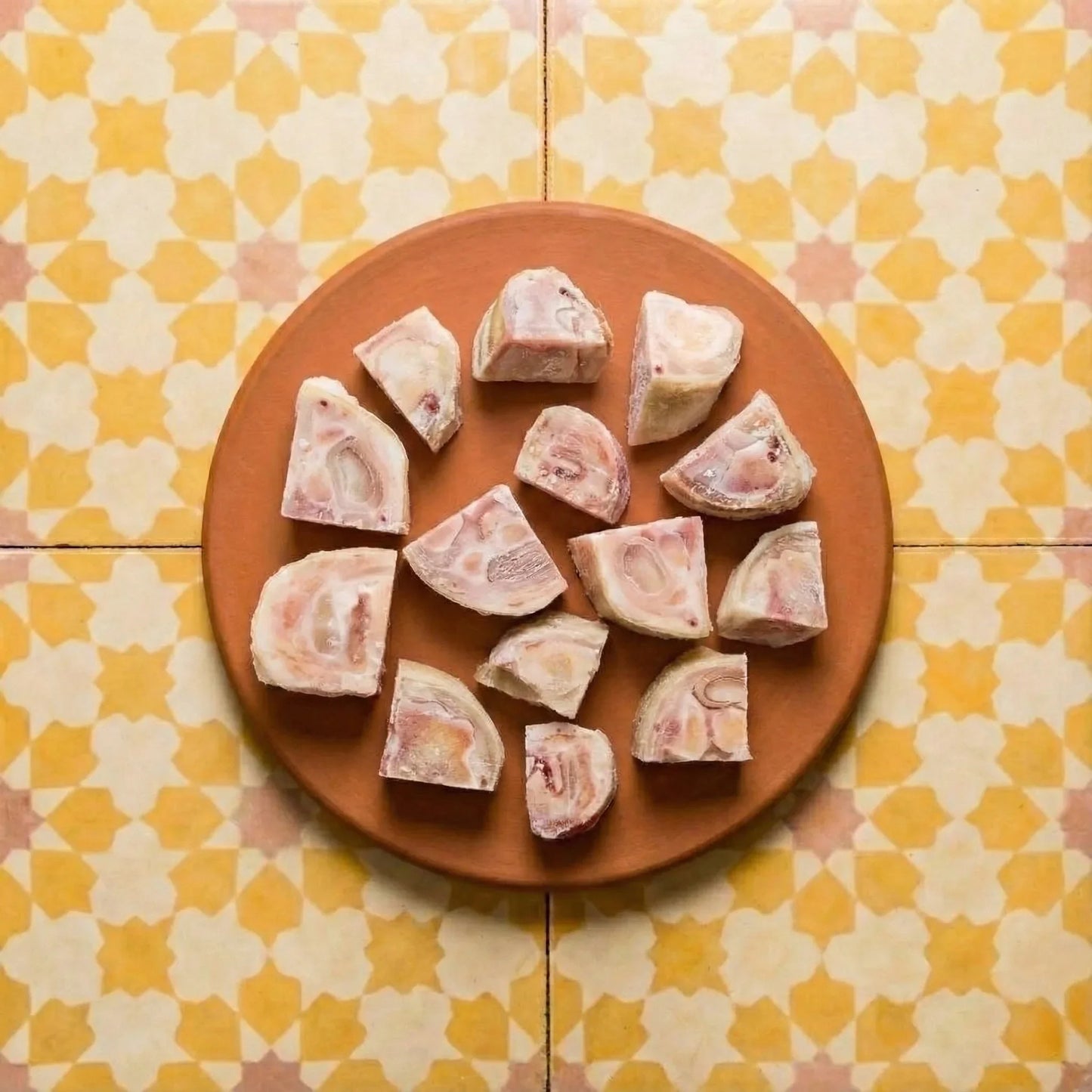Raw bone marrow pieces with pink and white marbling on a terracotta plate atop yellow and cream quadrifoil patterned tiles