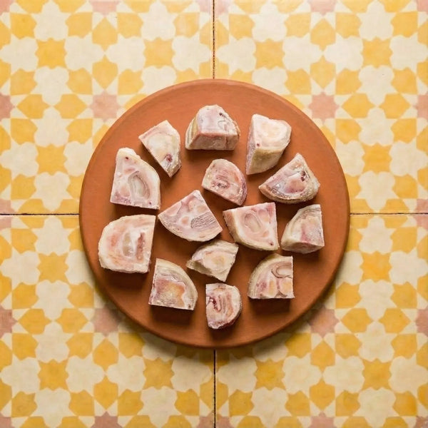 Raw bone marrow pieces with pink and white marbling on a terracotta plate atop yellow and cream quadrifoil patterned tiles