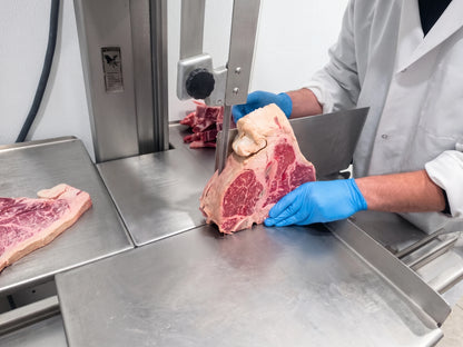Person in a meat processing plant using a band saw to cut T-bone steak.